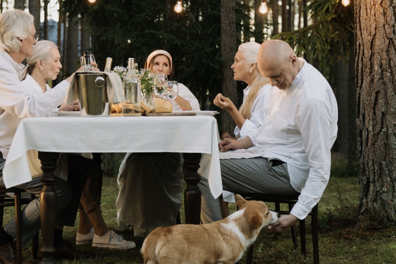 Family and friends dining outdoors under string lights with a corgi