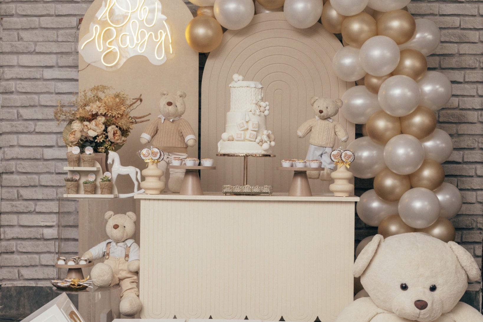 Neutral baby shower display with teddy bears, cake, and cream-and-gold balloons